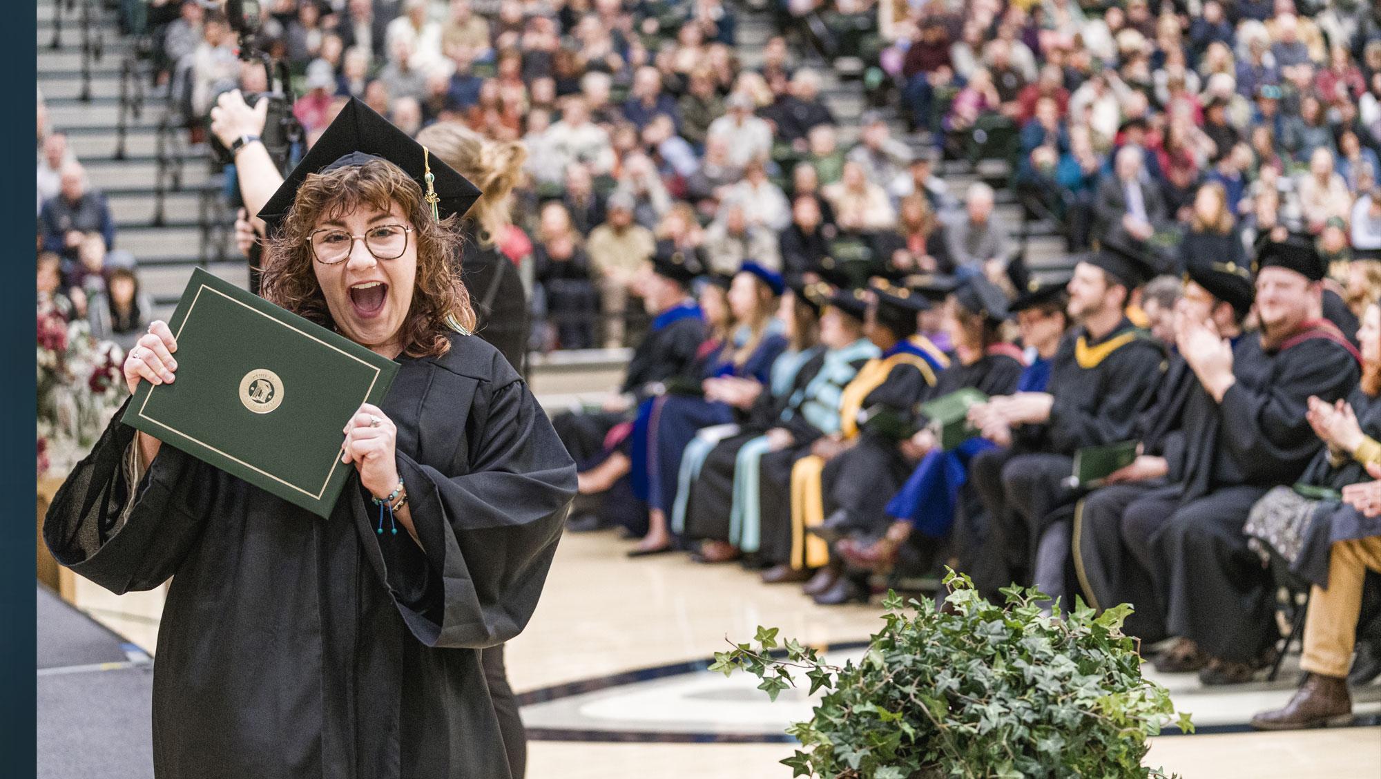 BHSU graduate poses smiling with degree at a commencement ceremony